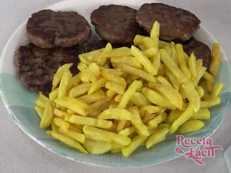 Hamburguesa jugosa de ternera sobre una tabla de madera con patatas alrededor