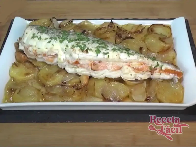 Merluza rellena con gambones y salmón ahumado sobre una cama de patatas y cebolla, plato principal navideño tradicional español